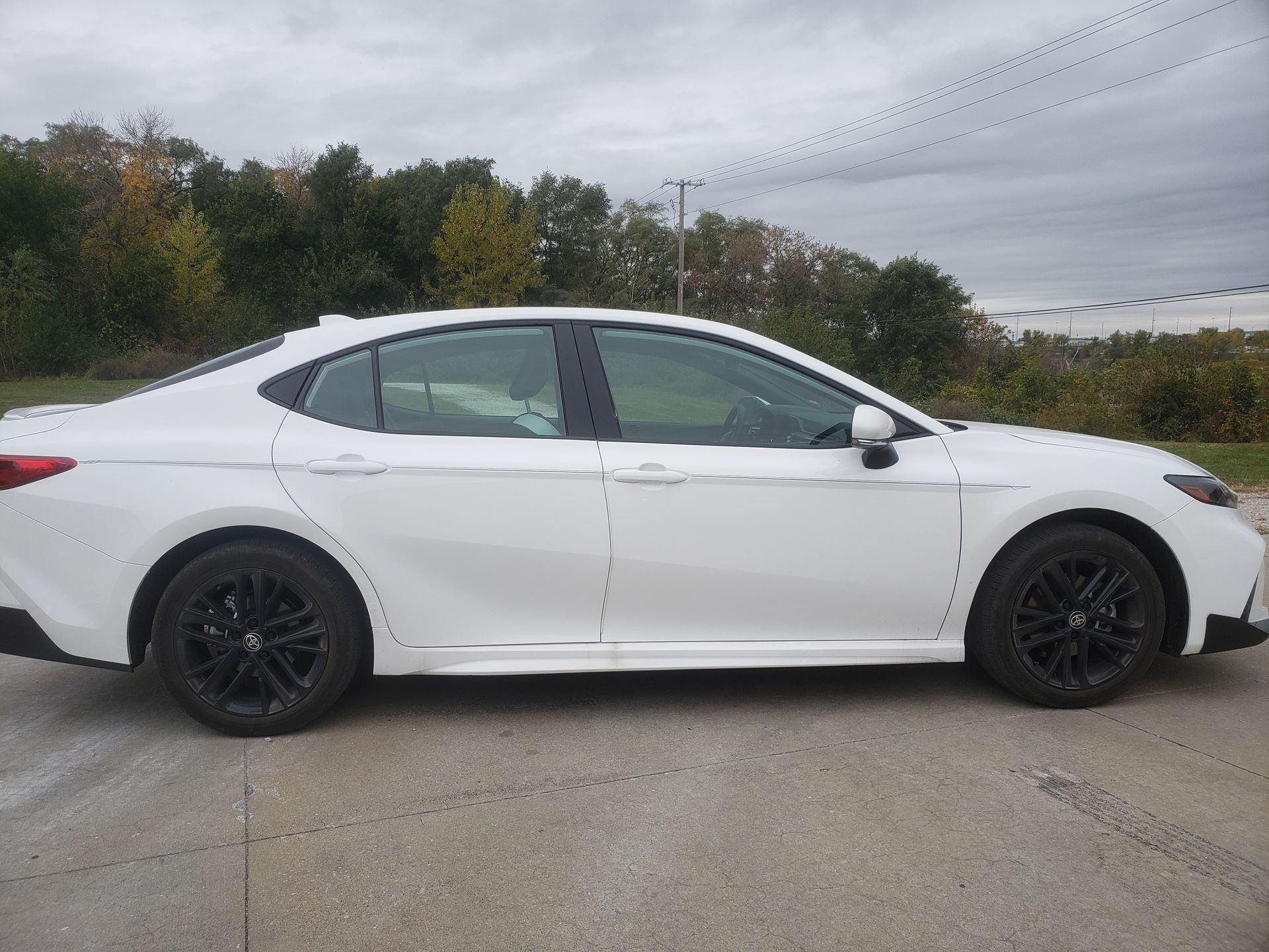 White Toyota Camry with black wheels, parked outdoors on a cloudy day.