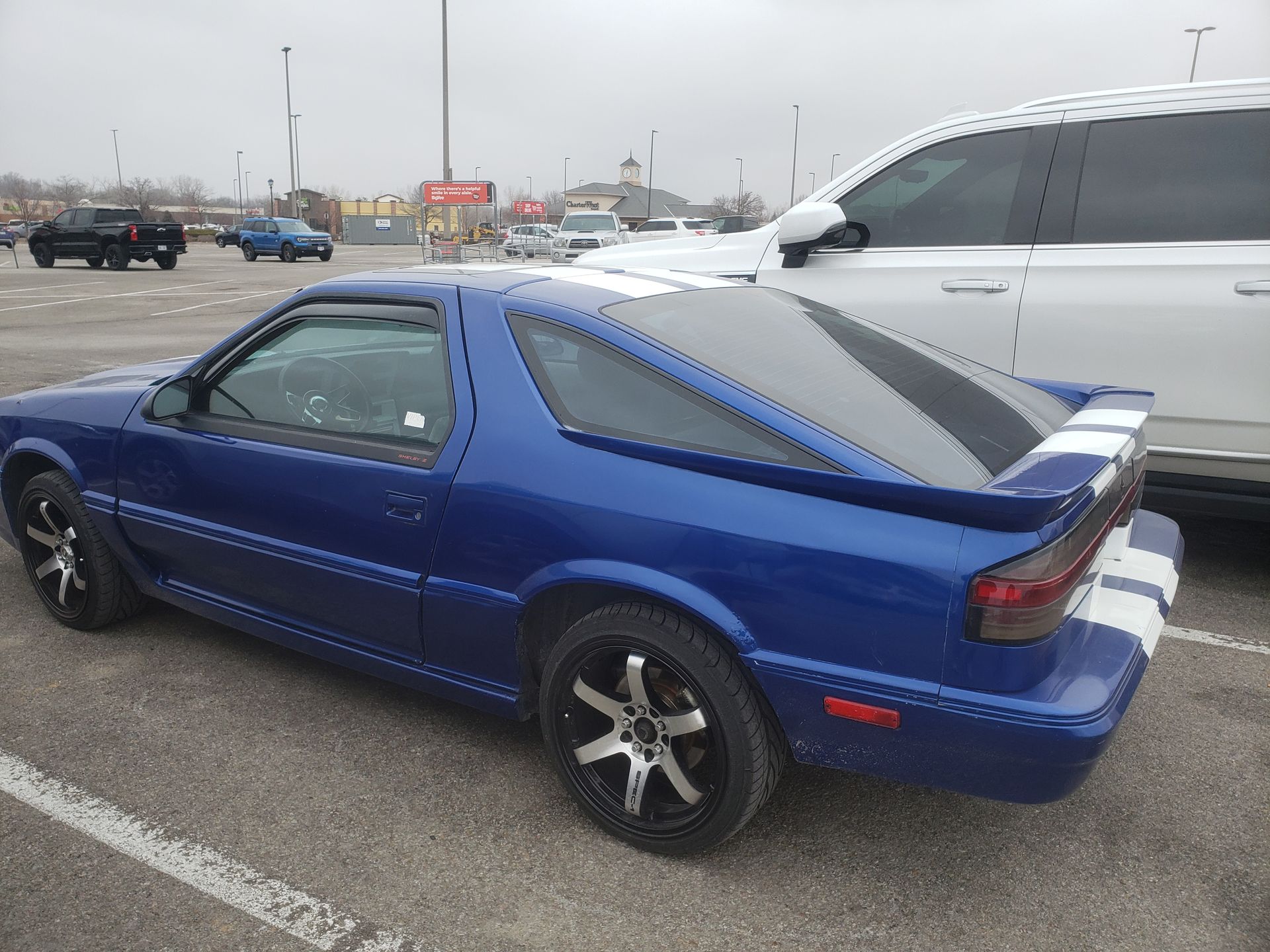 Blue Dodge Daytona with white racing stripes, parked in a lot.