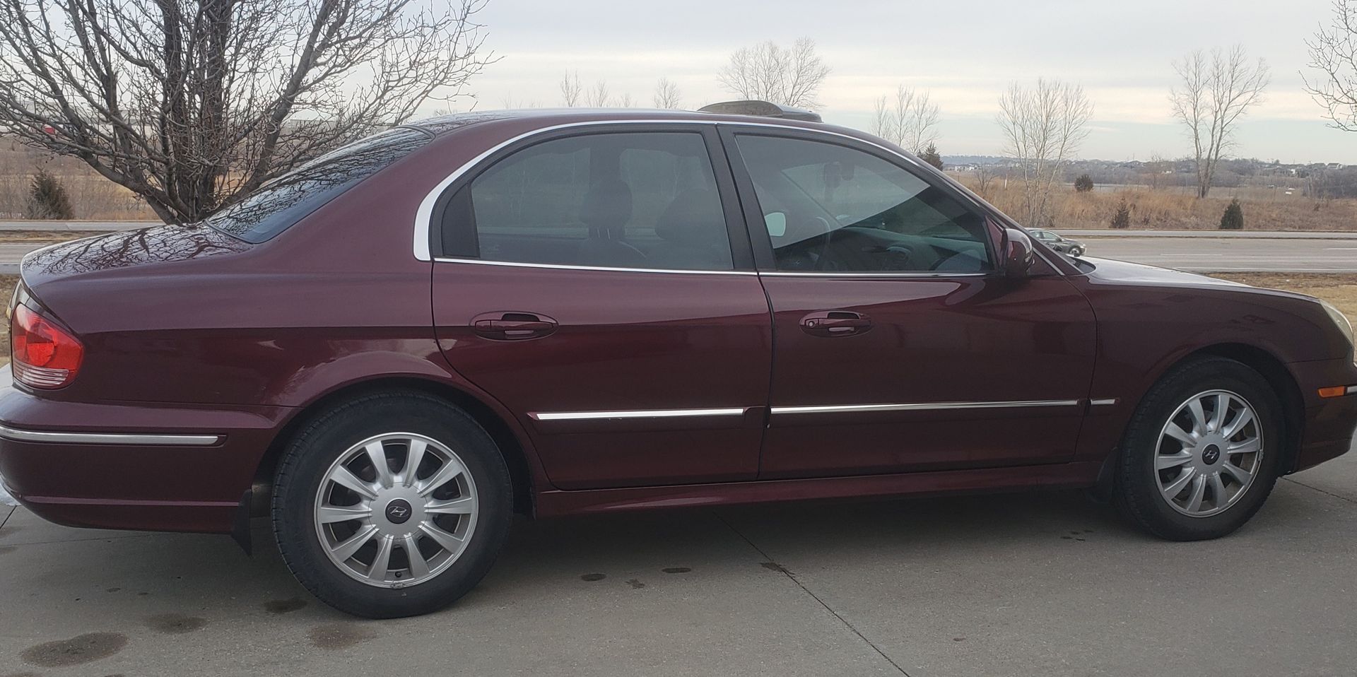A burgundy sedan parked on a concrete surface with a landscape in the background.