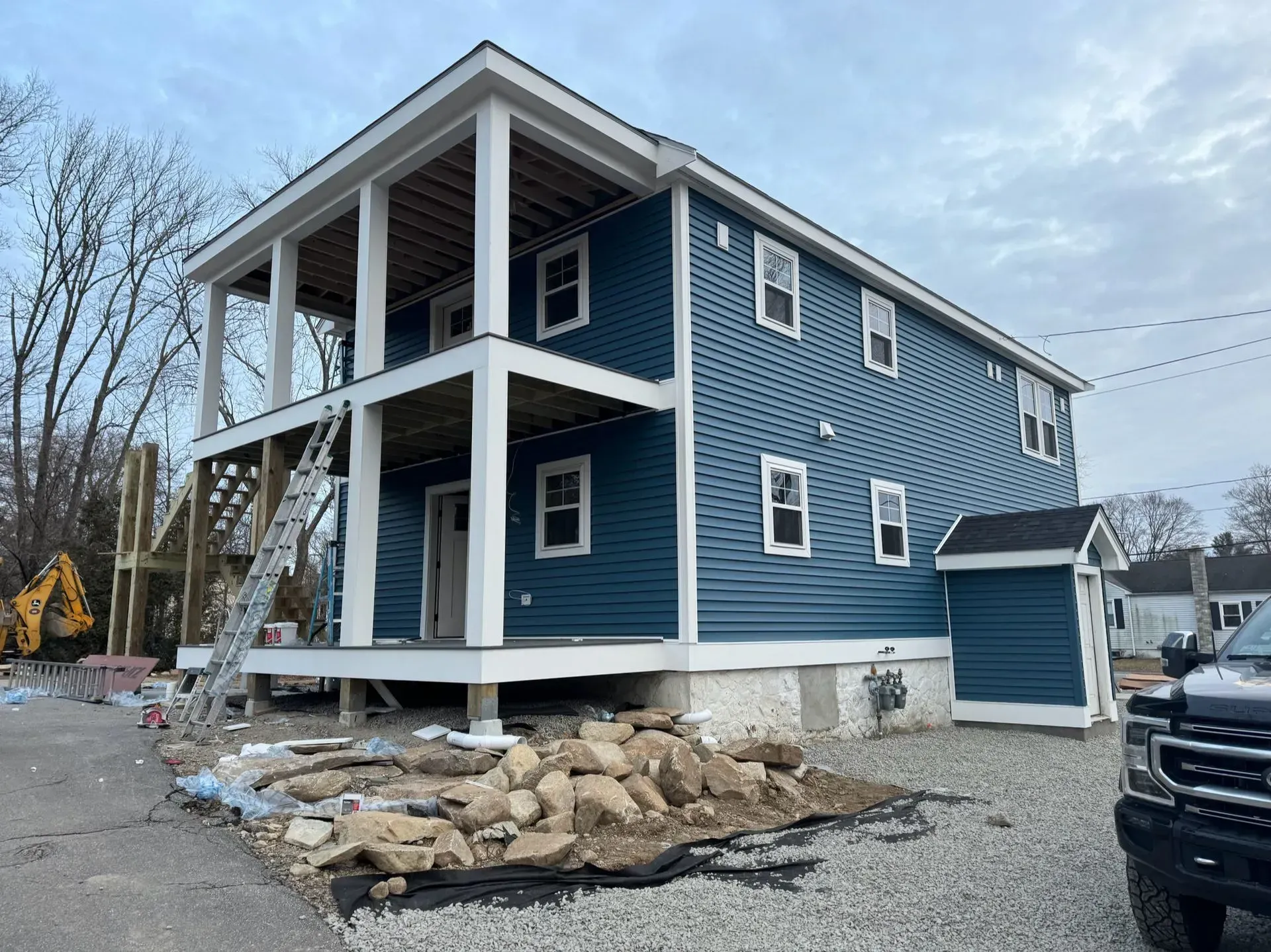 Two-story house under construction with blue siding, white trim, and a partially built porch.