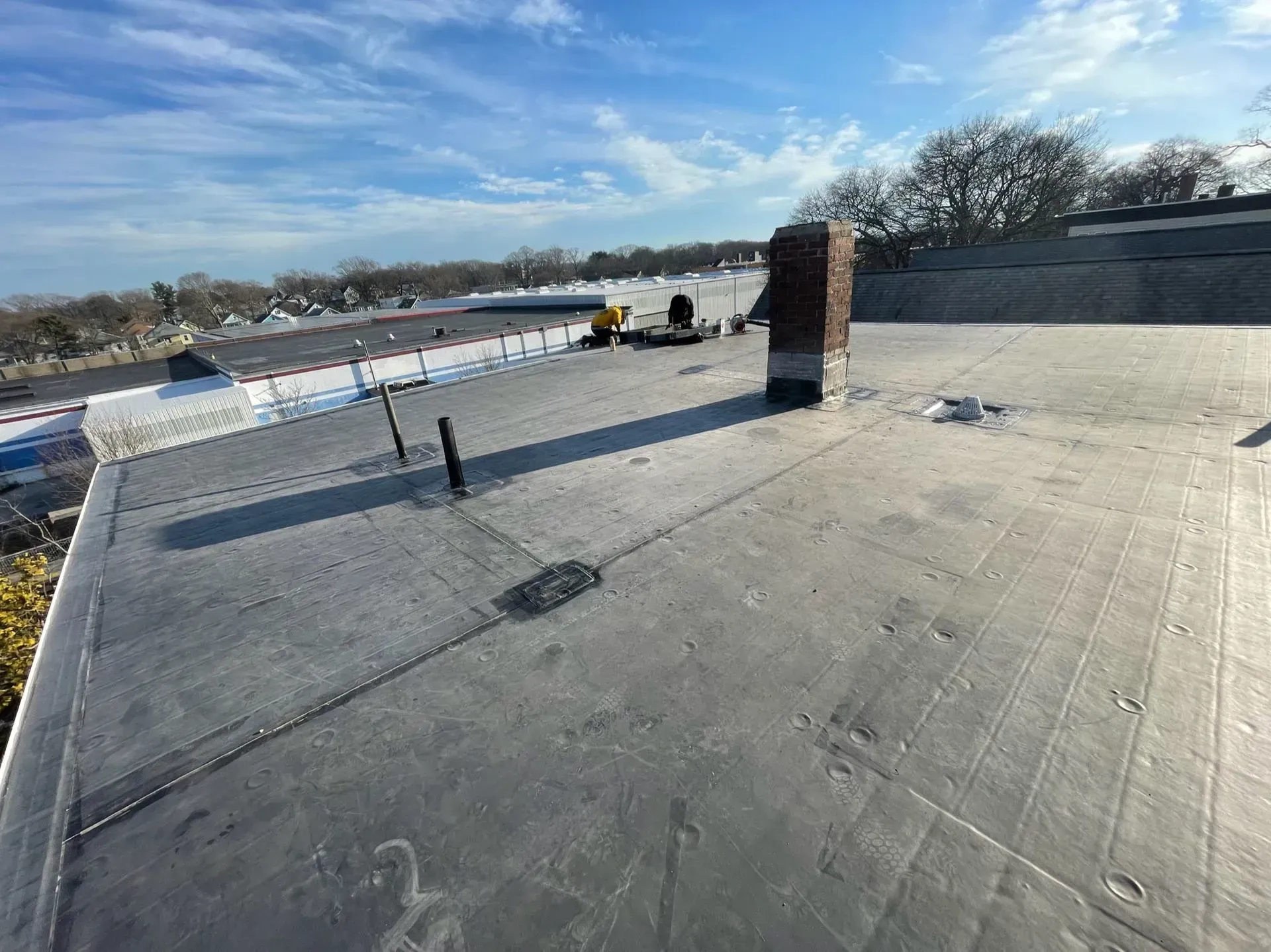 Flat rooftop with chimney, pipes, and equipment under a blue sky.