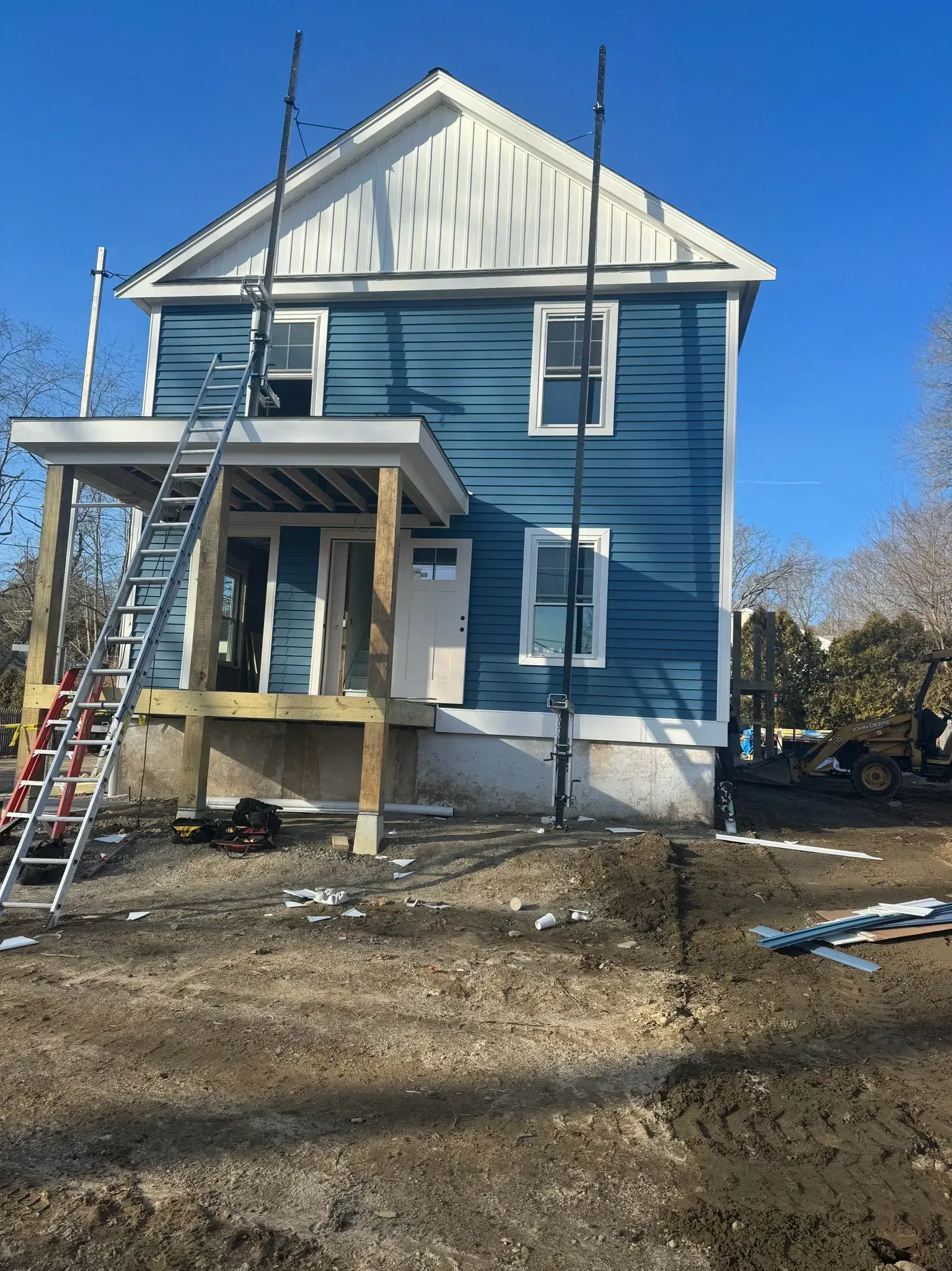 Blue two-story house under construction with scaffolding, porch, and a clear blue sky.