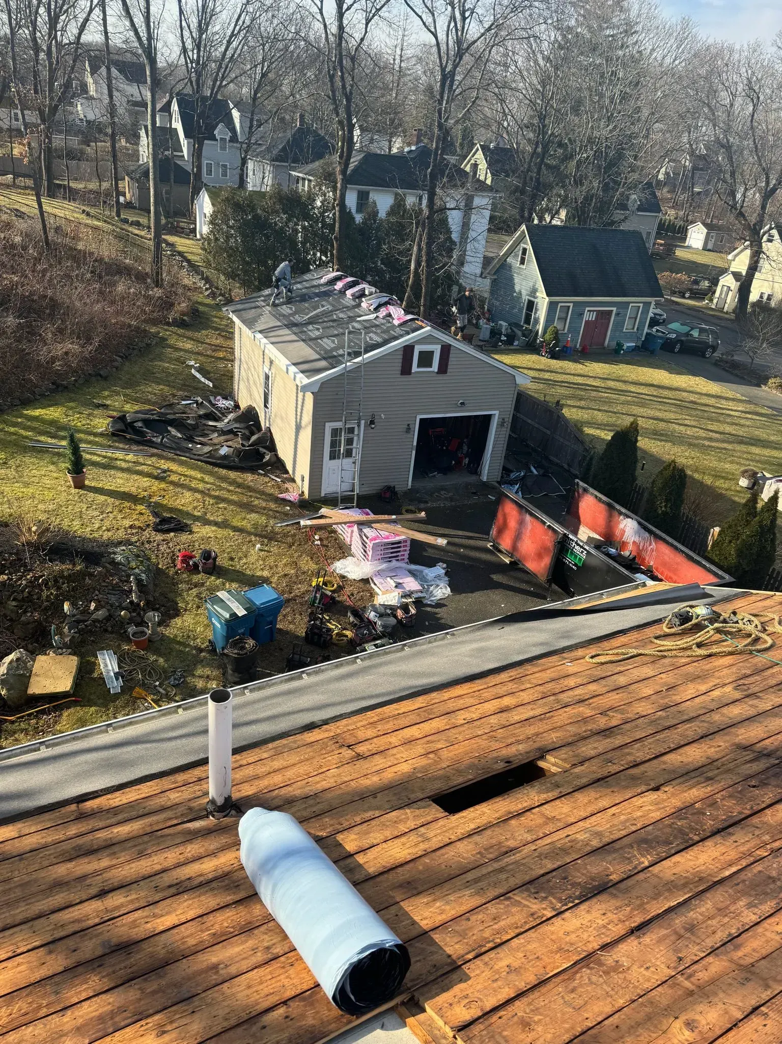 View from rooftop: a garage with open door, debris nearby, and houses in the distance on a sunny day.