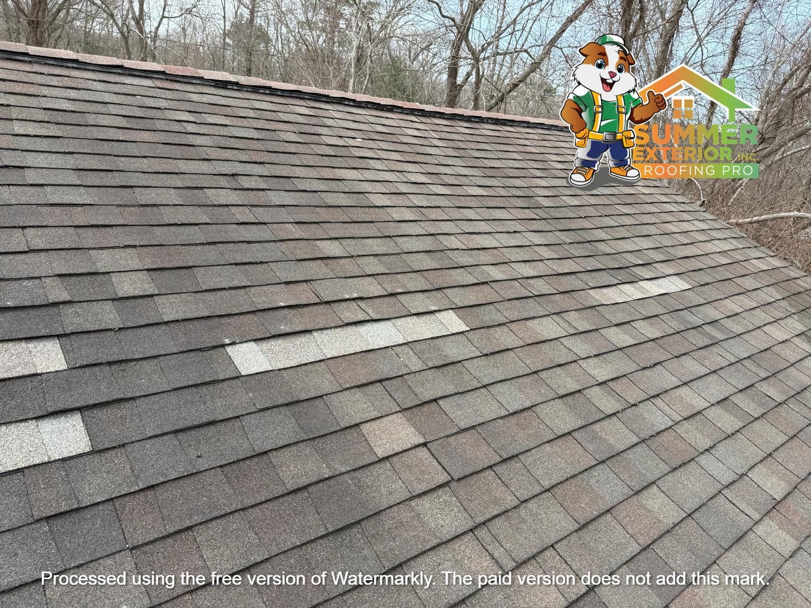 A pitched roof with asphalt shingles in shades of brown, featuring several missing shingles revealing the underlayment.