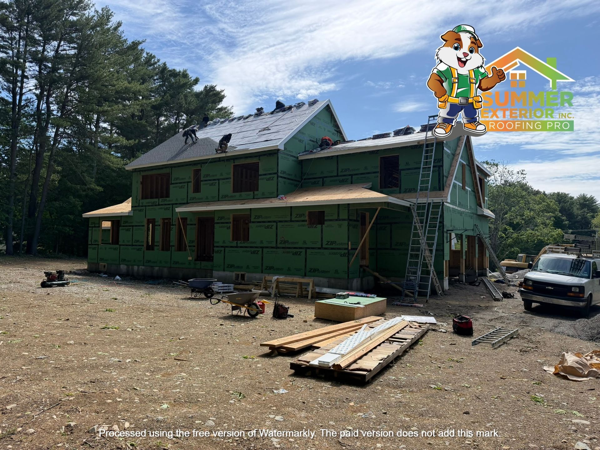 Green house under construction with scaffolding, lumber piles, and a truck in a wooded clearing.
