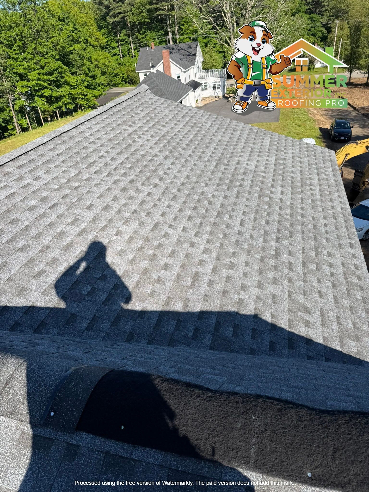 Rooftop with gray shingles and a shadow in front of green trees and a backyard playset