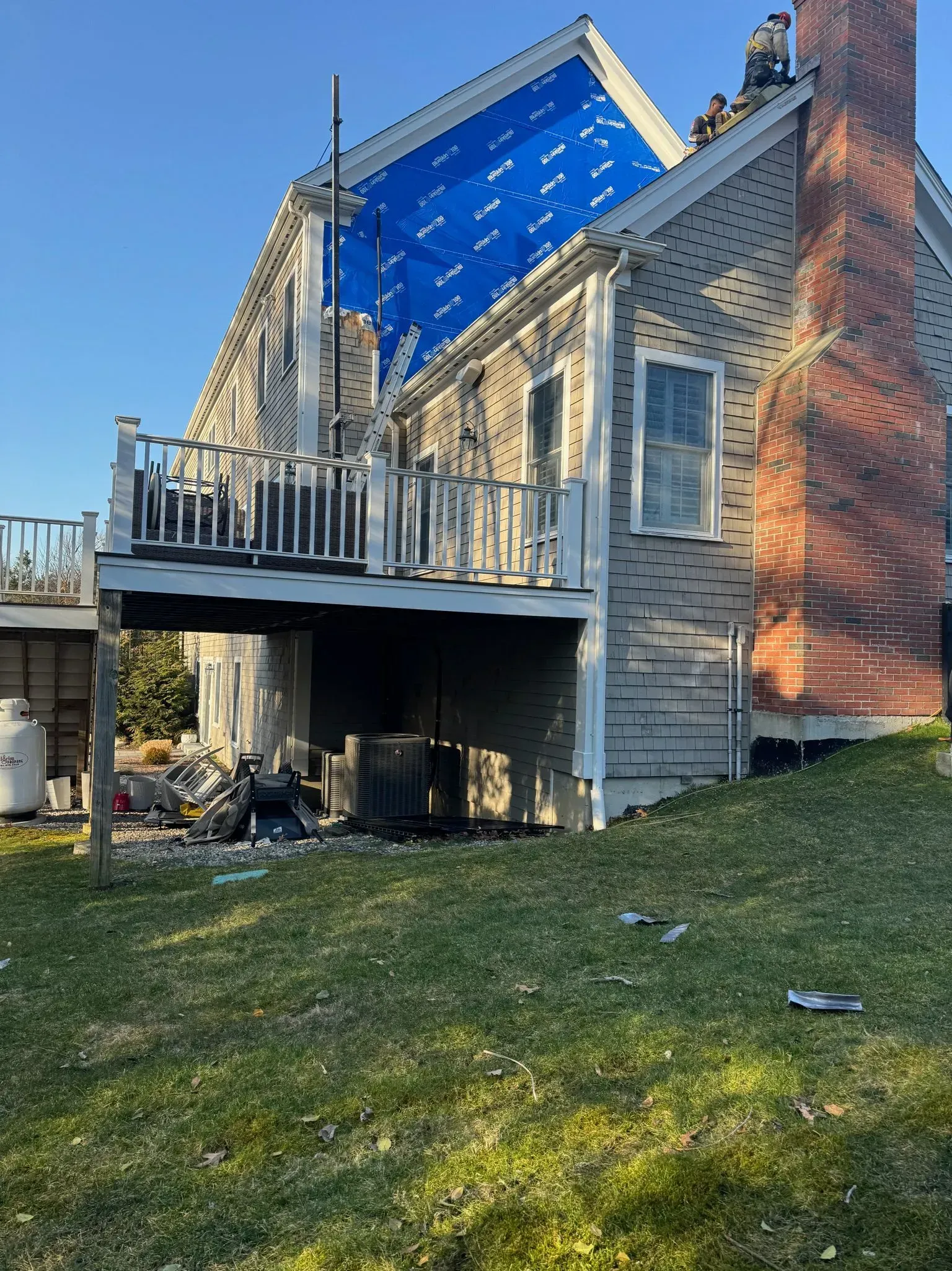 House with exposed roof covered by blue tarp, white siding, brick chimney, and deck.