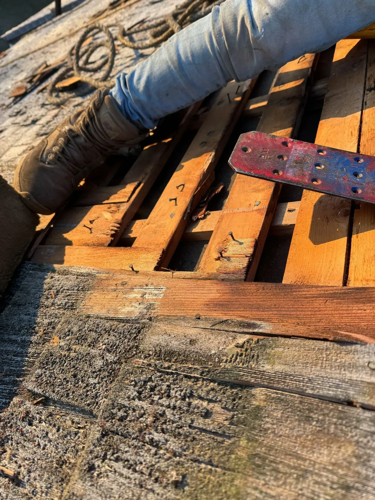 Rusted wood planks, and gray gravel. A blue and red tool, and a gray hose are present on the wood.
