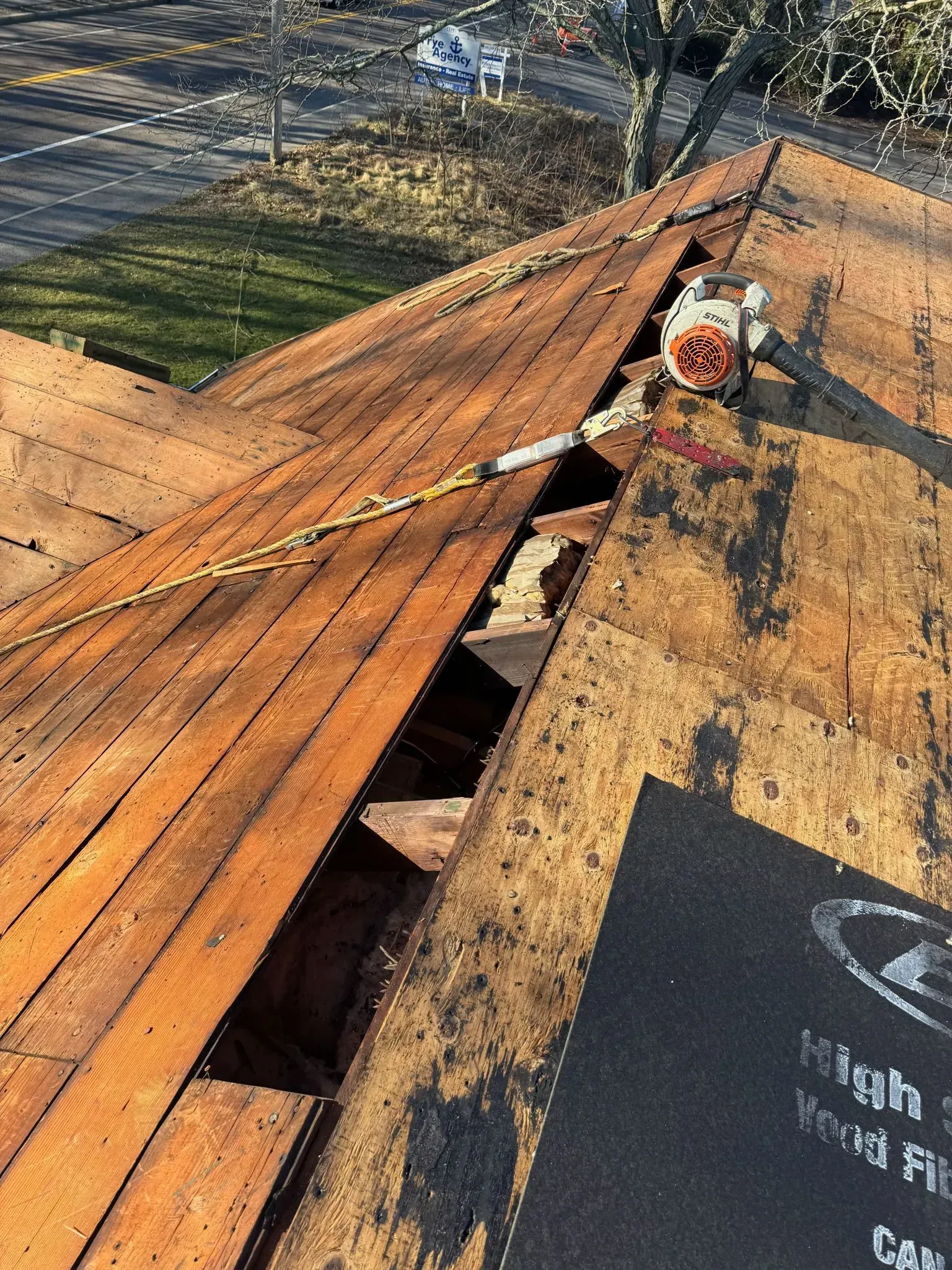 Rooftop with damaged shingles exposing underlayment. A power tool sits nearby.