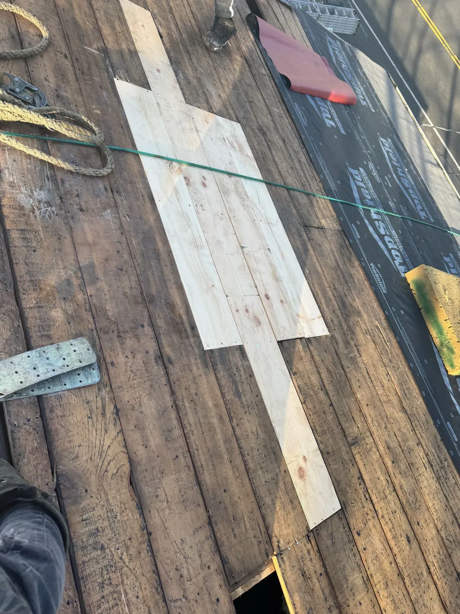 Wooden boards on a roof, creating a light-colored rectangular patch. A green rope and other roofing materials are visible.