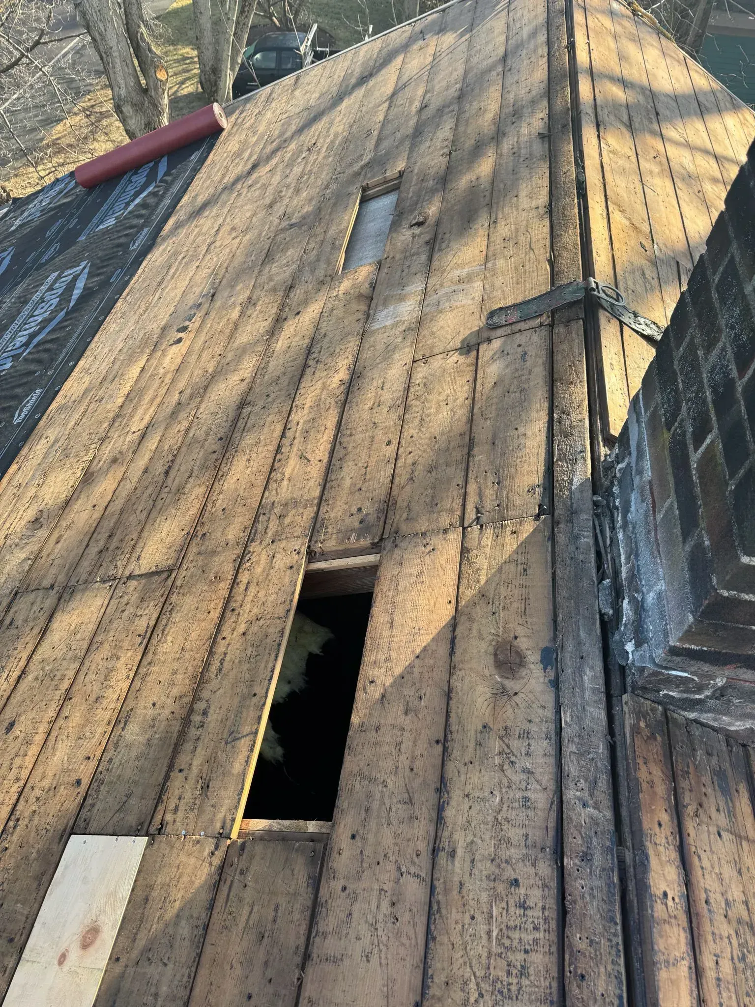 Damaged roof with exposed wood and holes. Chimney on the right.