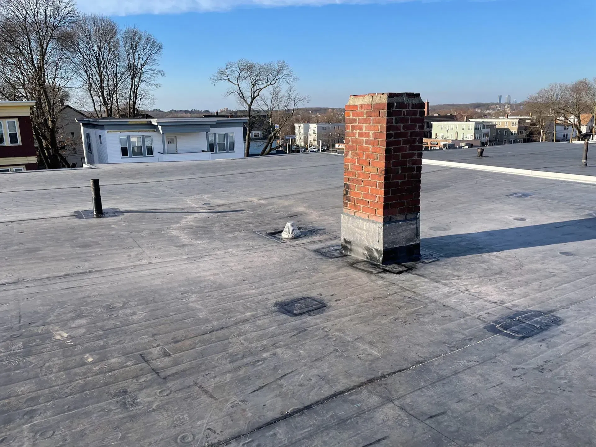 Rooftop with a brick chimney, patches, and a clear, sunny sky in the background.
