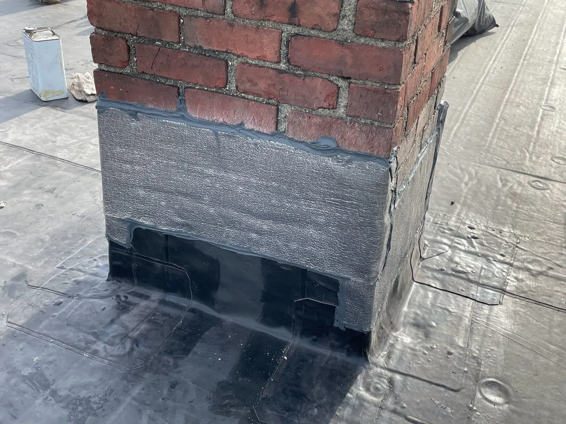 Brick chimney on a flat roof, sealed with dark roofing material.