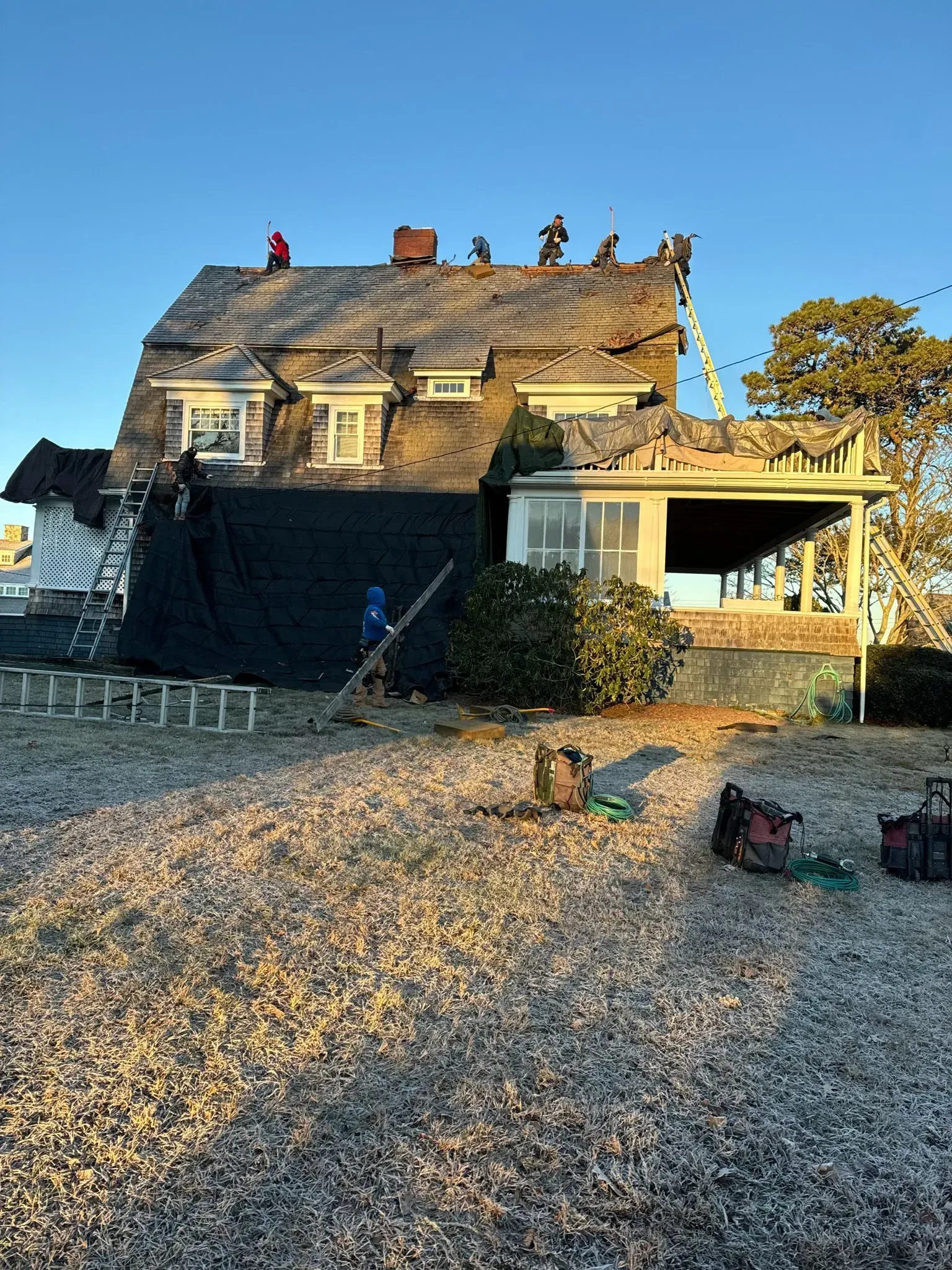 Workers on a rooftop, partially covered in black tarp, under clear, blue skies.