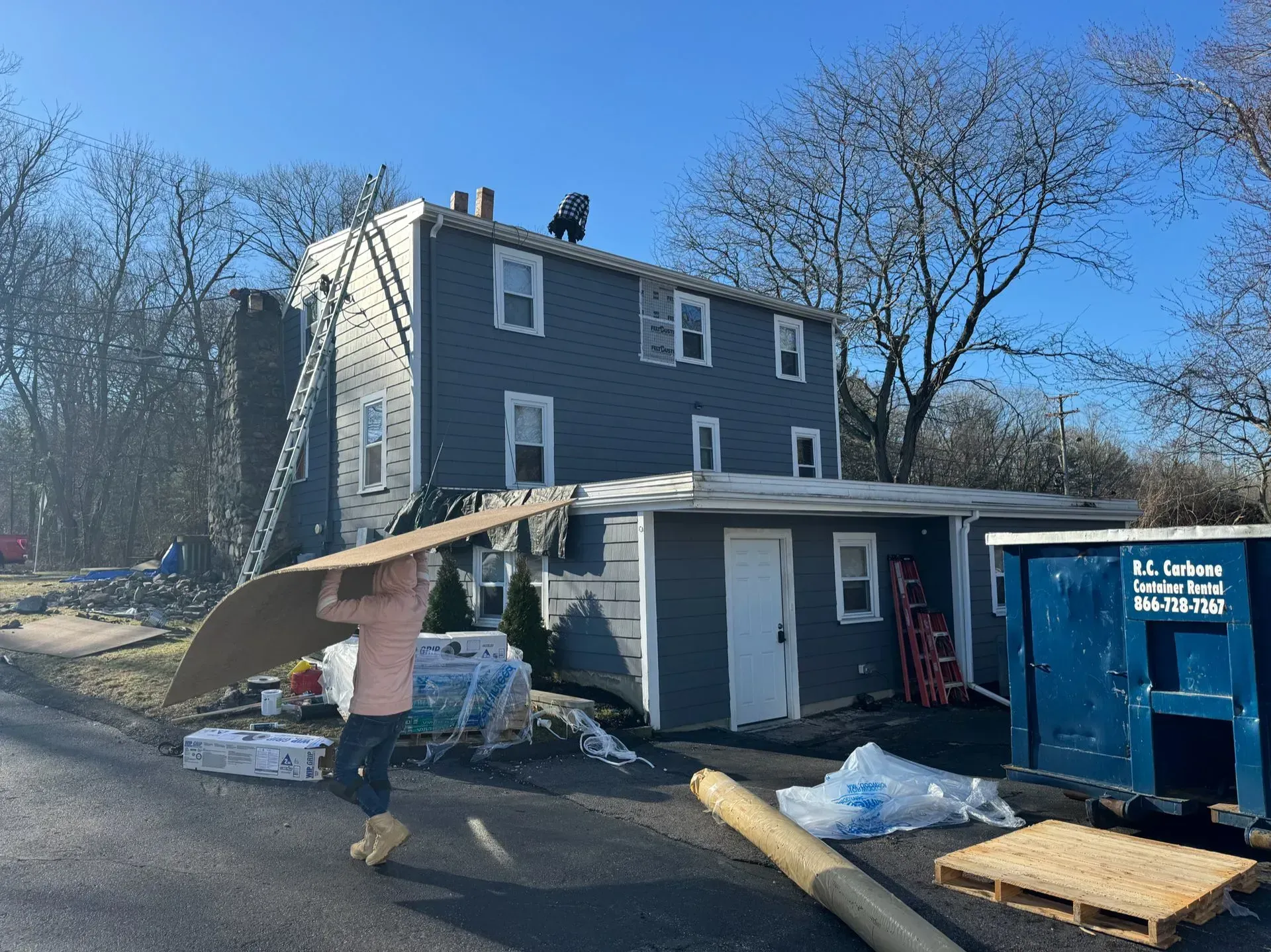 Construction workers on a roof, another carrying cardboard. Building exterior in the daytime.