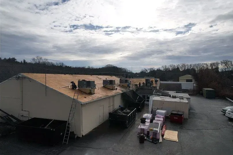 Workers on a flat roof with stacks of roofing materials, under a cloudy sky.