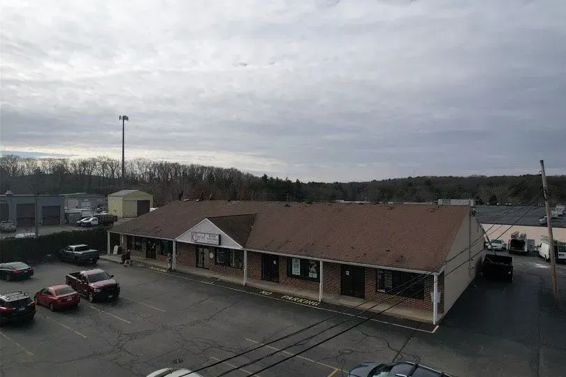 Brown-roofed, single-story building in a parking lot on a cloudy day. Cars parked in front.