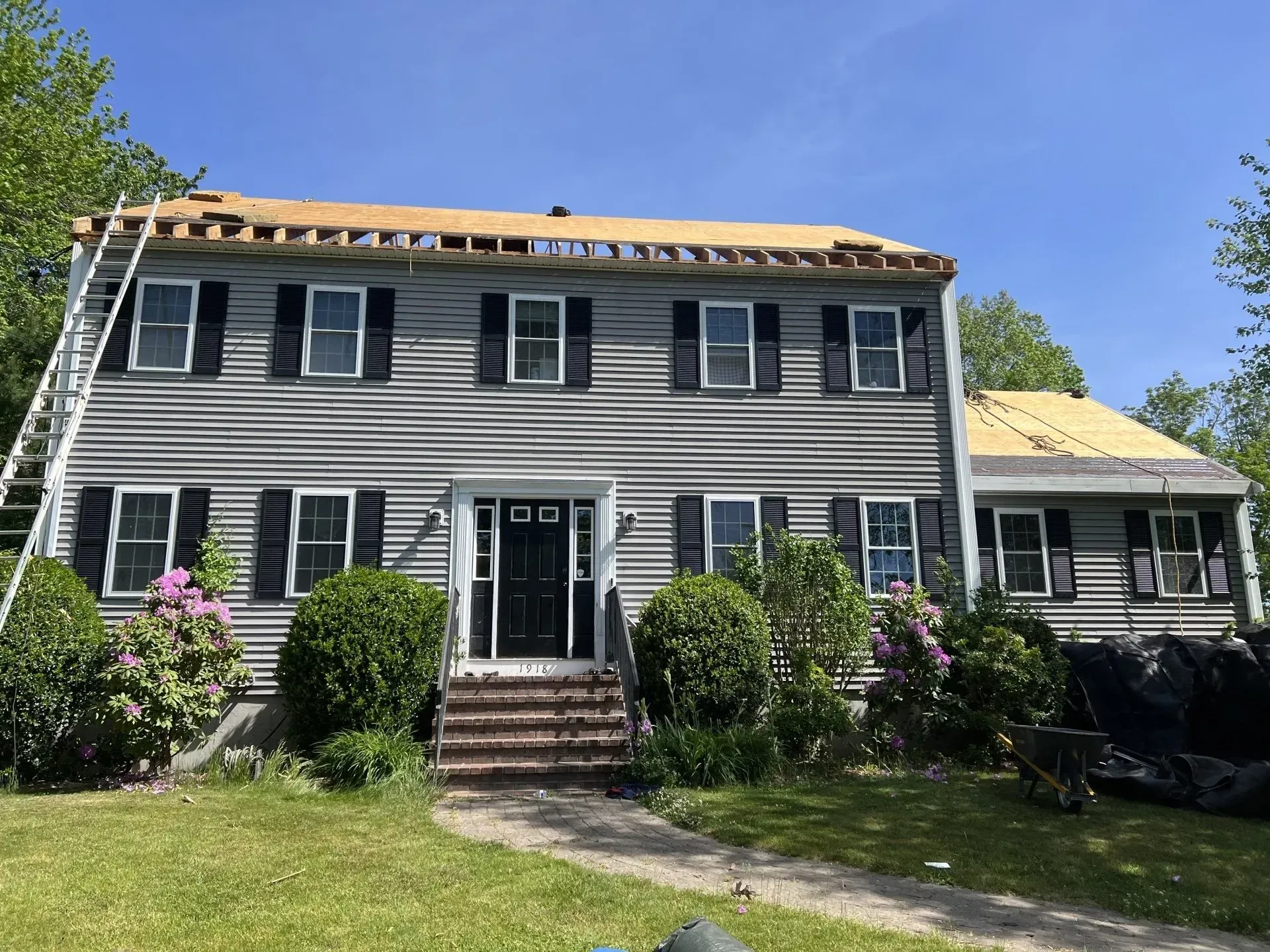House with roof partially removed, ladder leaned against the siding, blue sky.