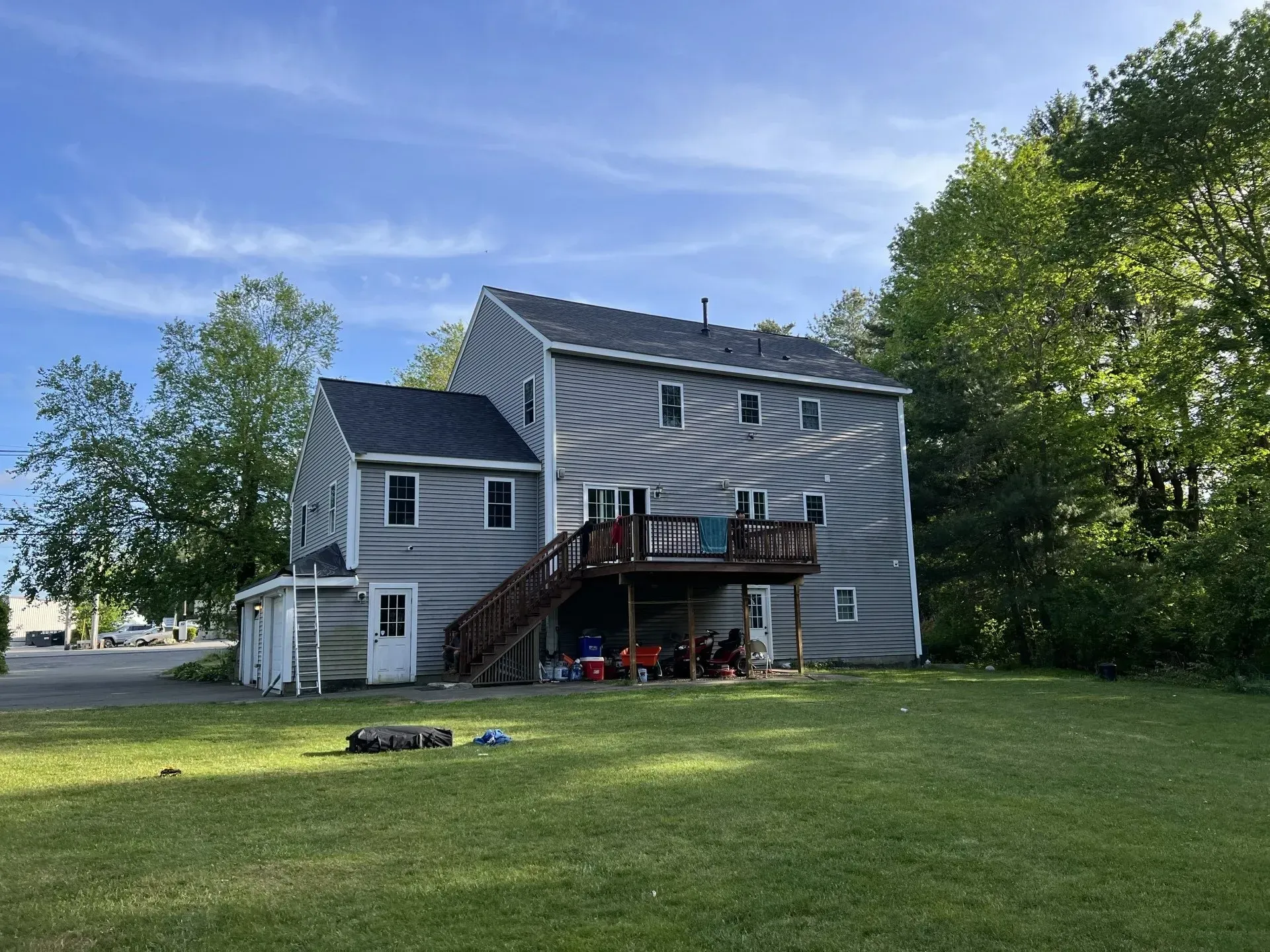 Two-story gray house with deck, surrounded by trees and grass, under a blue sky.