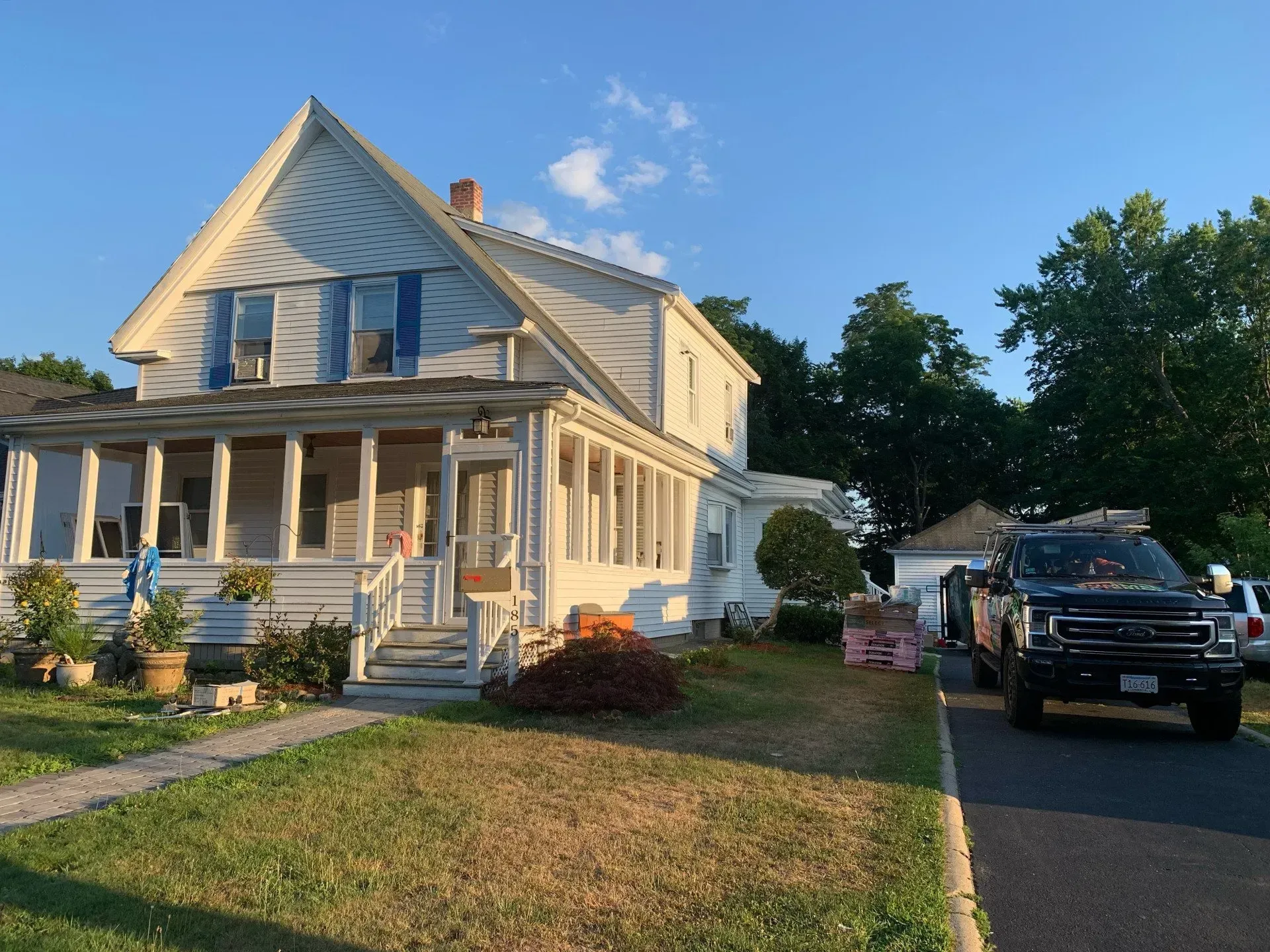 White house with porch and blue shutters; black truck in driveway on sunny day.