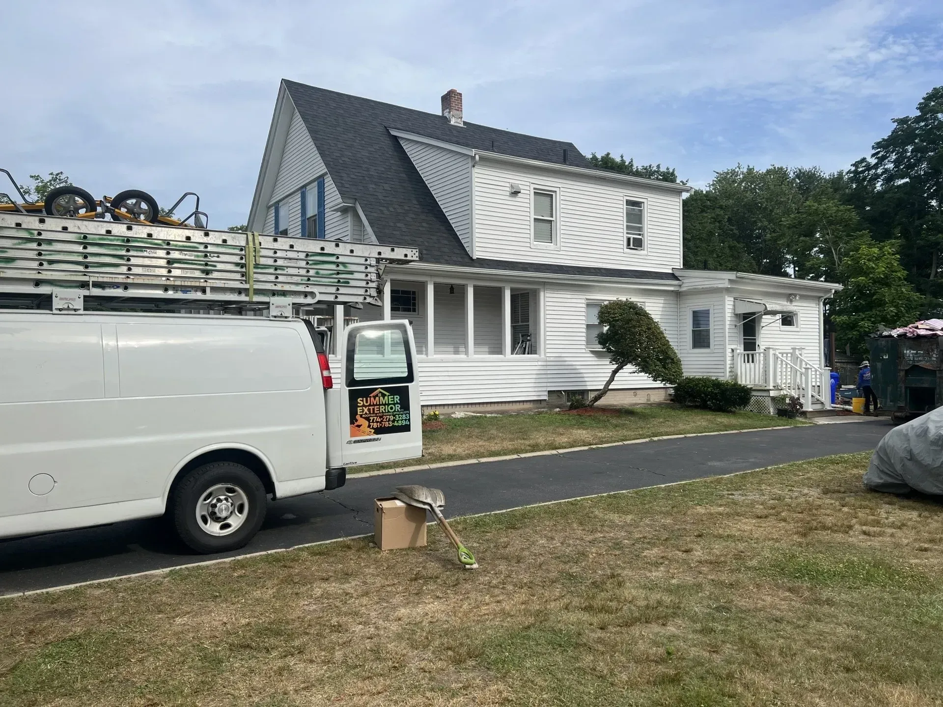 White van parked by a white house with a dark roof; tools and ladder visible.