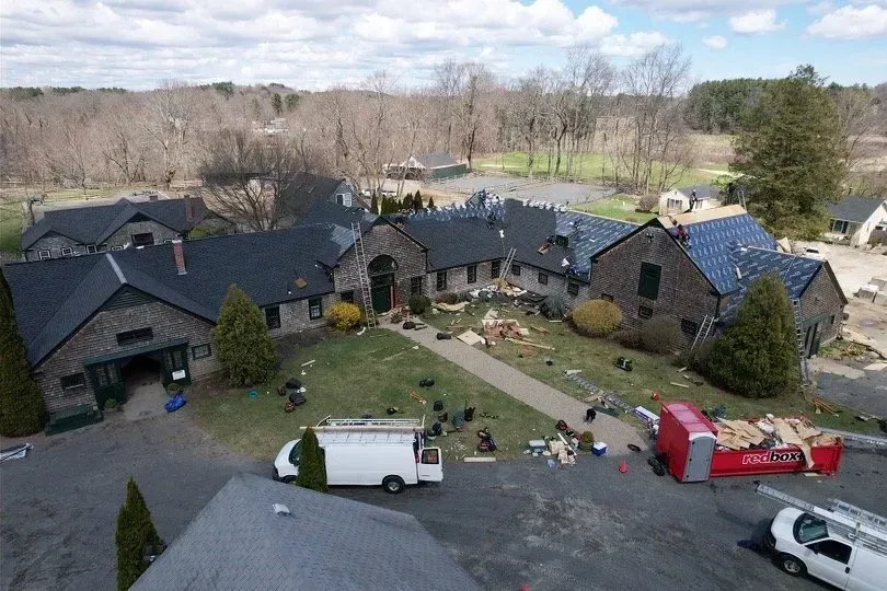 Aerial view of a complex roof replacement in progress on a multi-building structure with workers and materials visible.