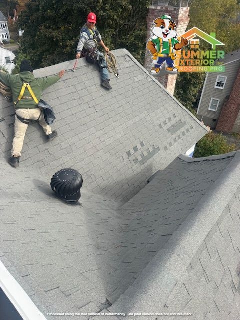 Roofers working on a gray shingle roof, one is roped up, another walking. Summer Exterior logo visible.