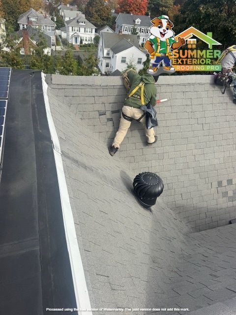 Roofer working on shingled roof, attached to safety harness. Solar panels and residential neighborhood in background.