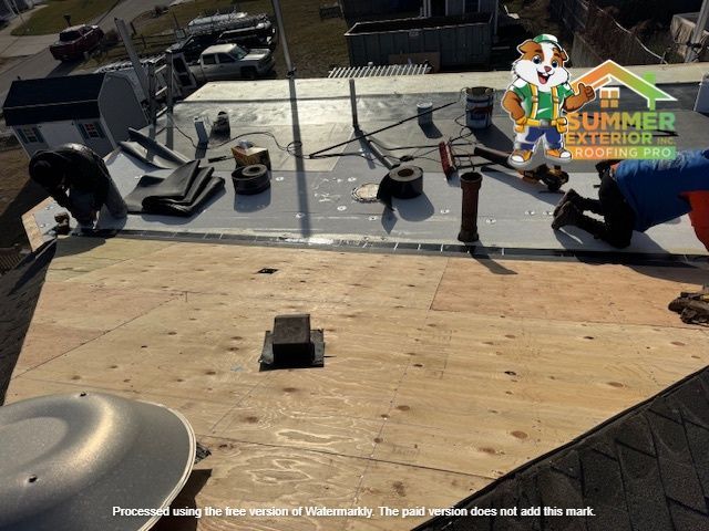 Roofers working on a flat roof, applying roofing material. Summer Exteriors logo visible.