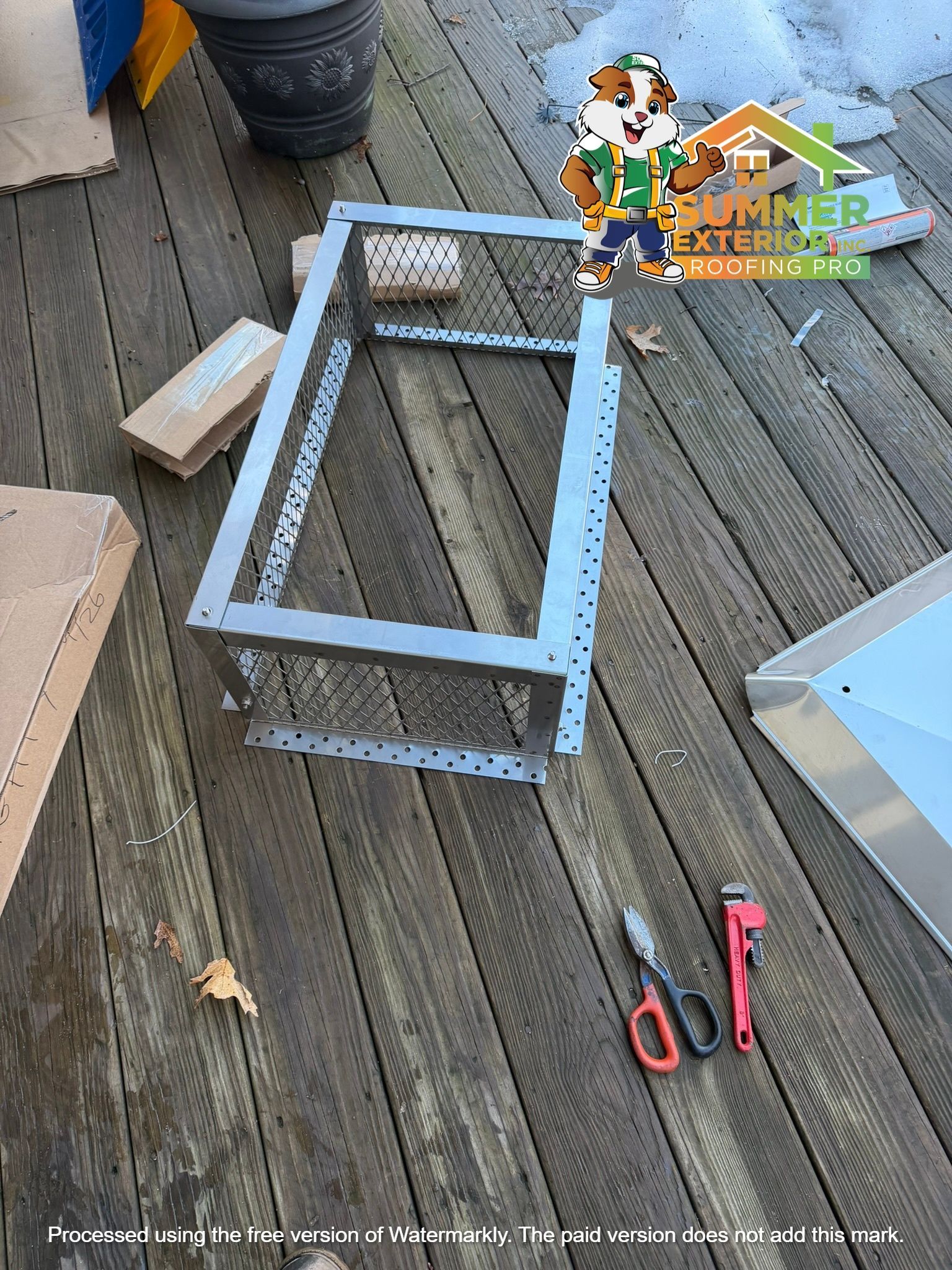 A metal frame on a wooden deck with hand tools nearby, including tin snips and a wrench, during a DIY construction project.