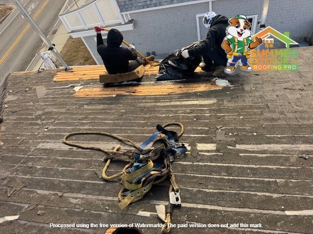 Roofers working on a residential roof, one is using a sled to remove debris. Safety harness on the roof.