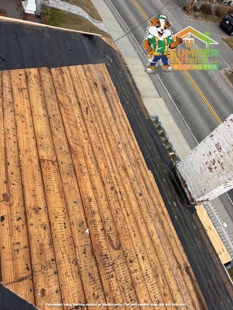 Wooden roof boards with black underlayment, and a chimney next to a street with a mascot.
