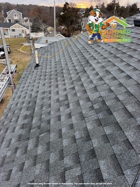 View of a gray shingle roof on a house, featuring the Summit Roofing Pro logo with a cartoon dog.