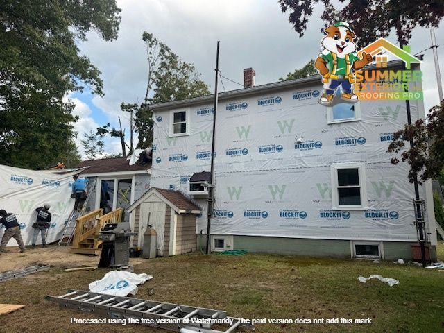 Workers installing weather barrier on a house. Green and blue wrap covers the walls.