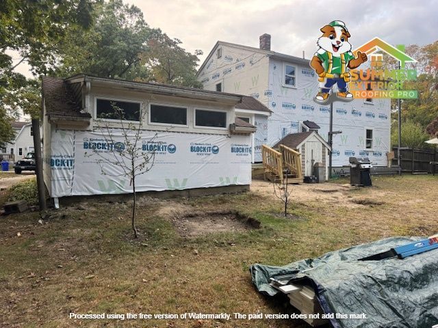 Exterior of a house under construction; white protective wrap, mascot logo, and grassy yard.