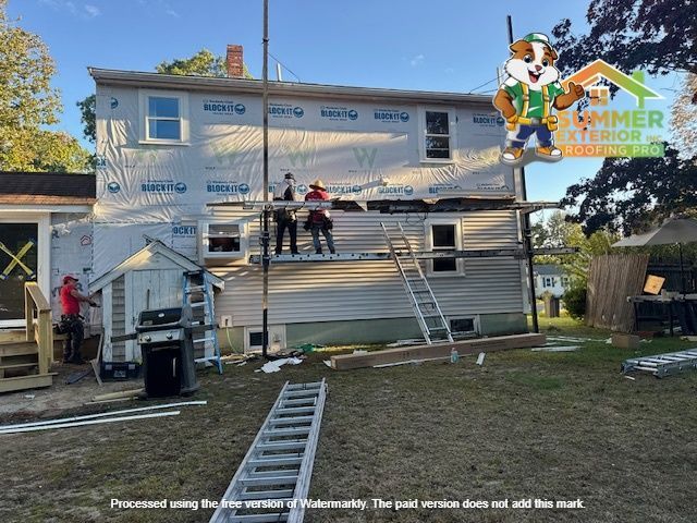 Workers installing siding on a two-story house, using scaffolding. Green lawn, blue sky, and company logo in corner.