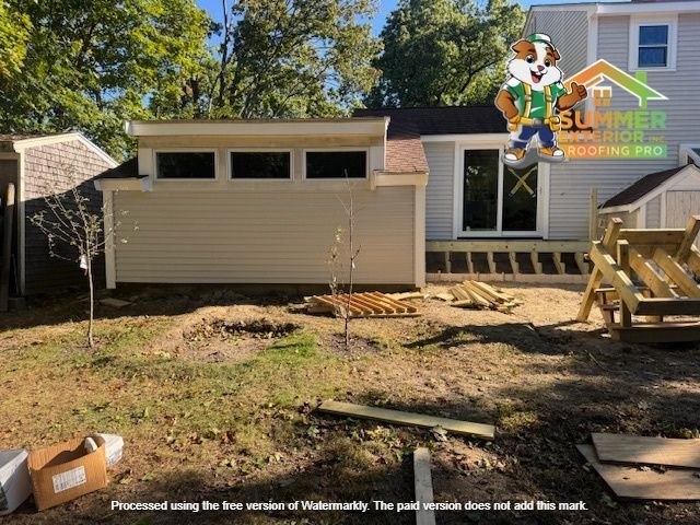 Backyard with new beige building, small shed, and construction materials on the ground.