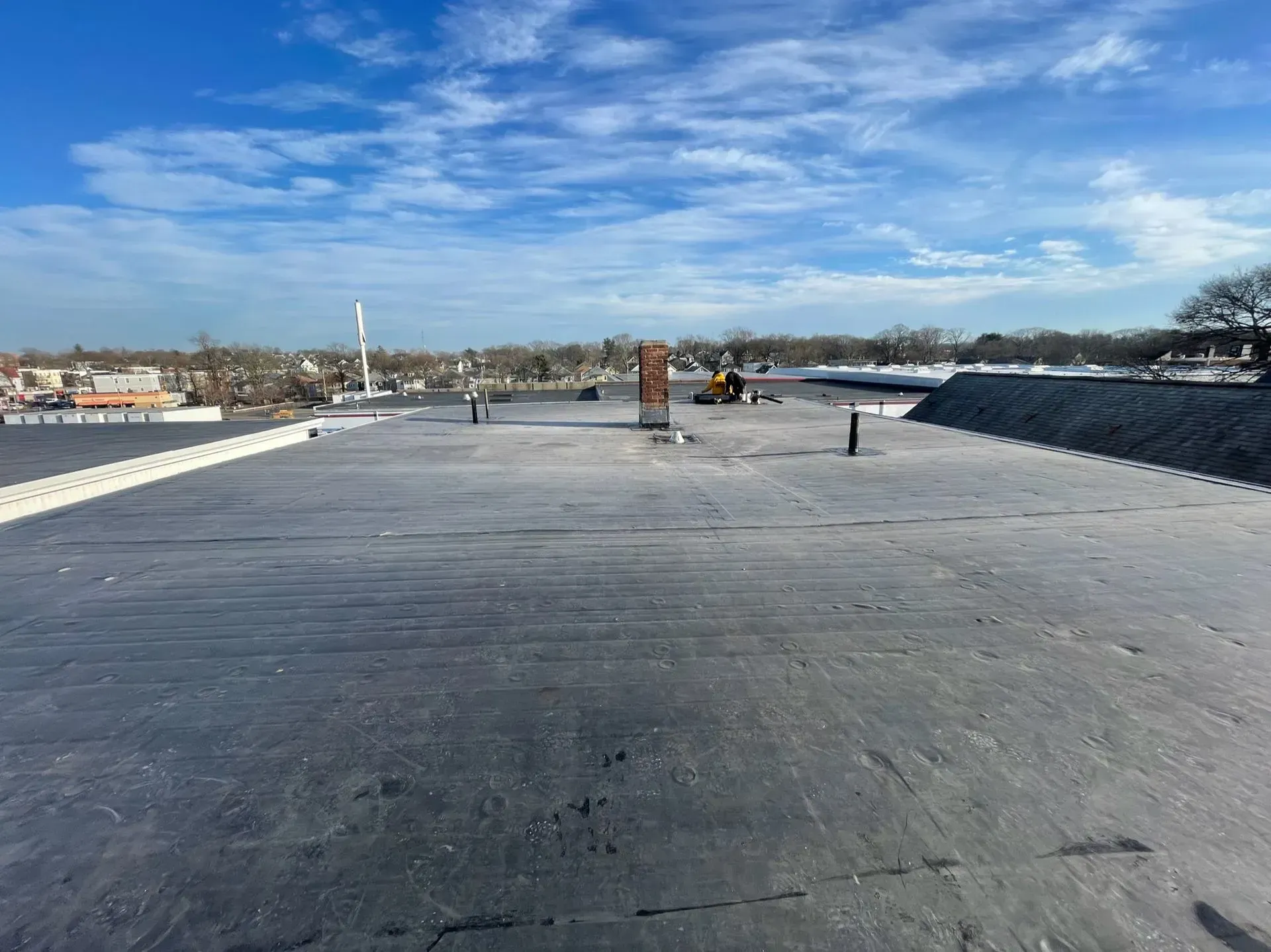 View of a flat, black commercial roof on a sunny day. A few vents and a worker are visible.