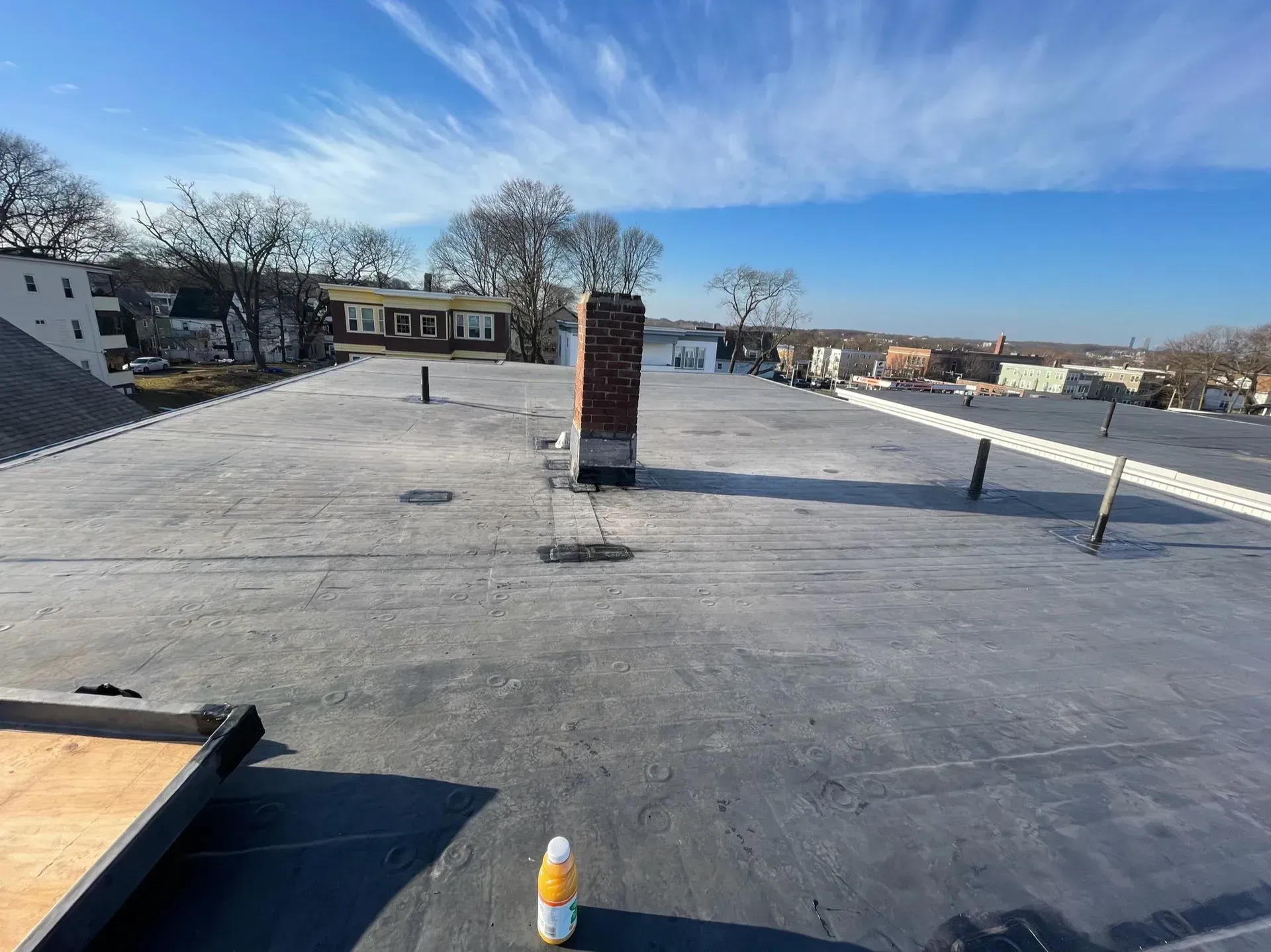 Flat rooftop with brick chimney, clear sky, distant buildings, and utility fixtures.