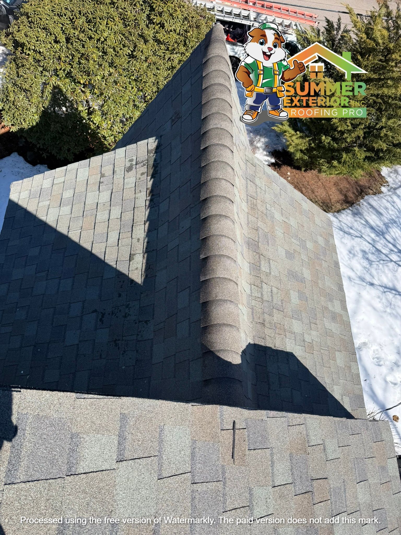 An aerial view of a dark grey asphalt shingle roof with a prominent ridgeline and a logo for Summer Exteriors.