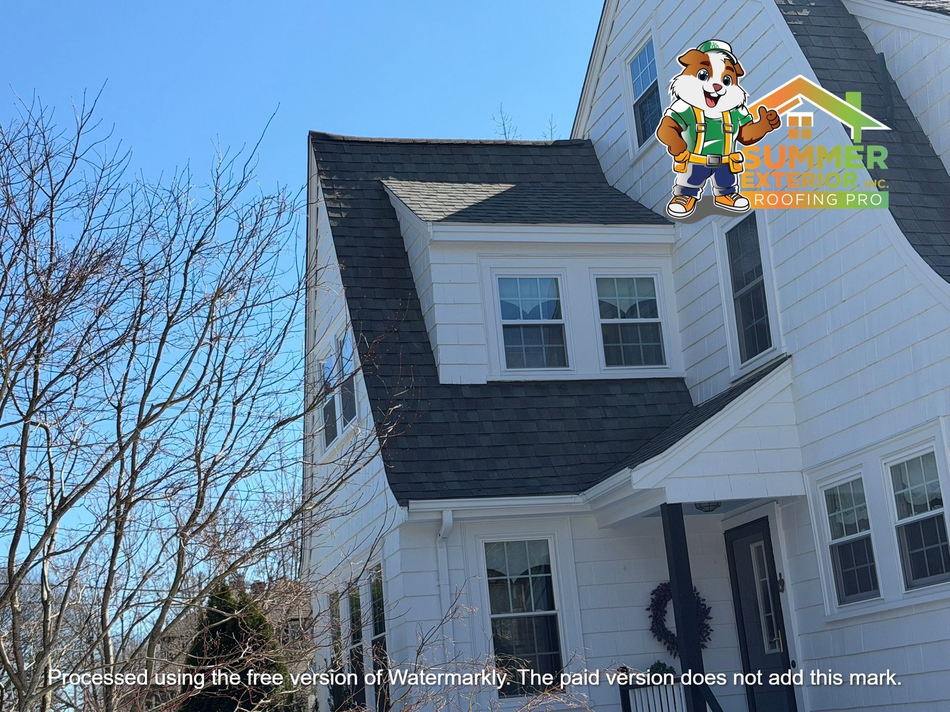 A white house with a steep gray shingled roof, a dormer window, and a small porch against a bright blue sky.