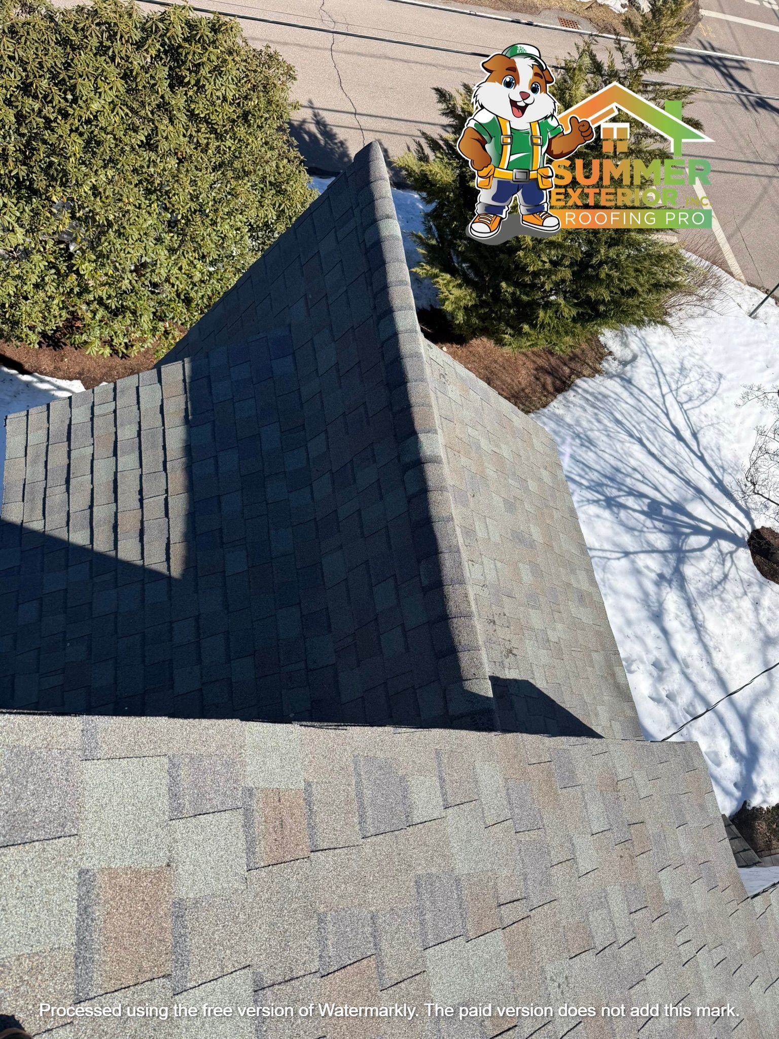 An aerial view of a dark shingled residential roof with a company logo in the corner.