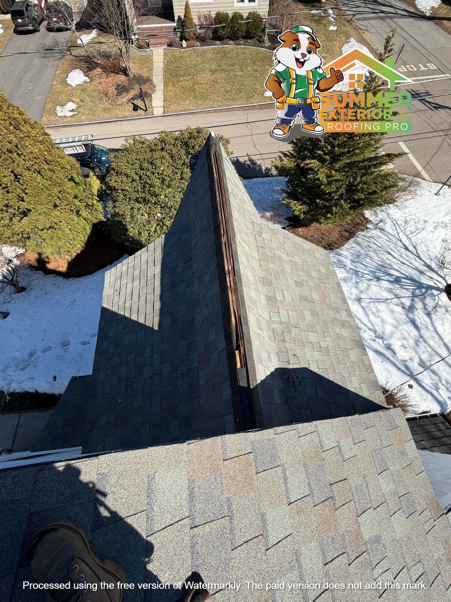 High-angle view of an asphalt shingle roof with a valley and a brand logo in the upper right corner.