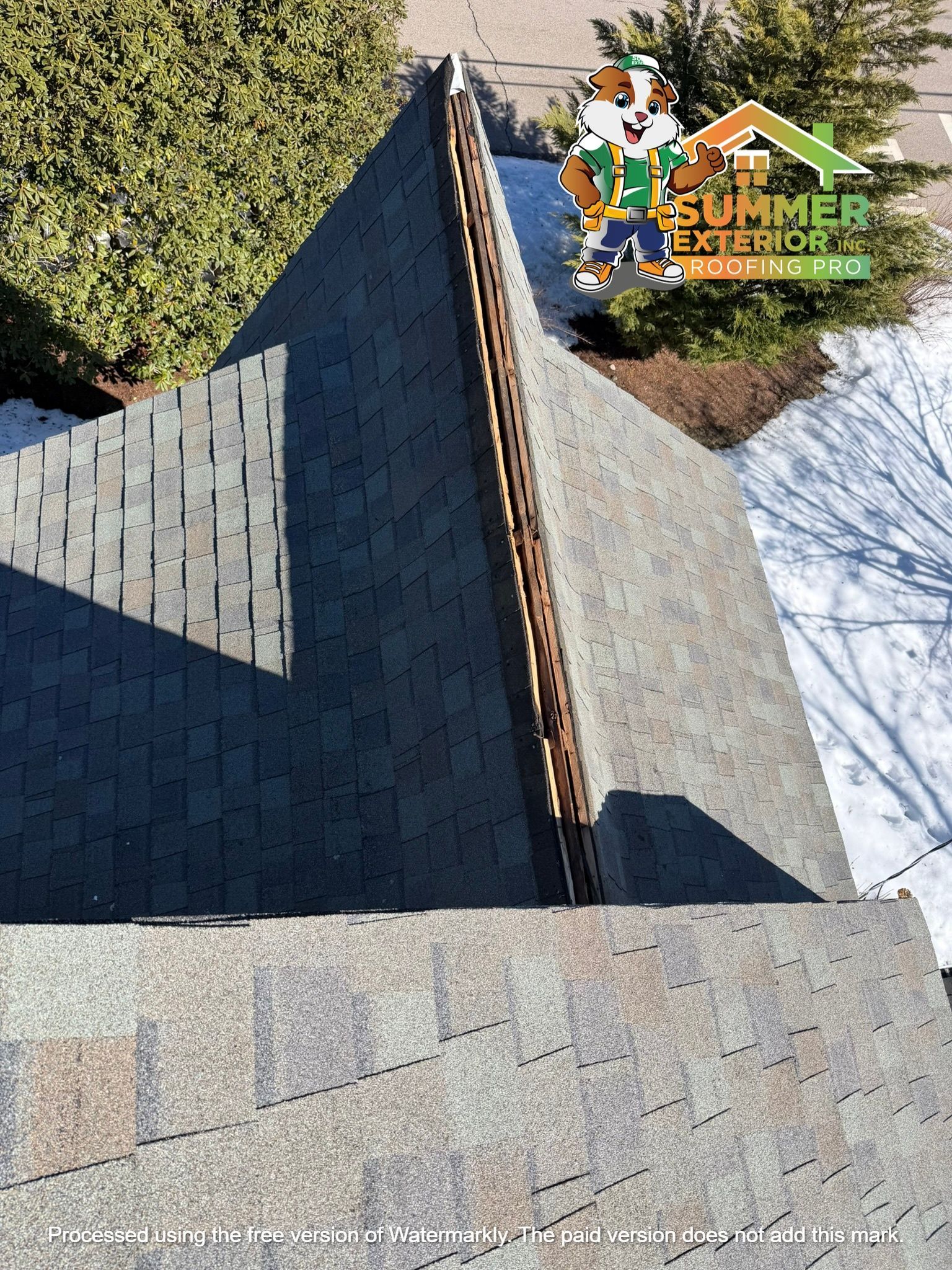 Aerial view of a gray asphalt shingle roof featuring a ventilated ridge cap, with a logo in the top right corner.