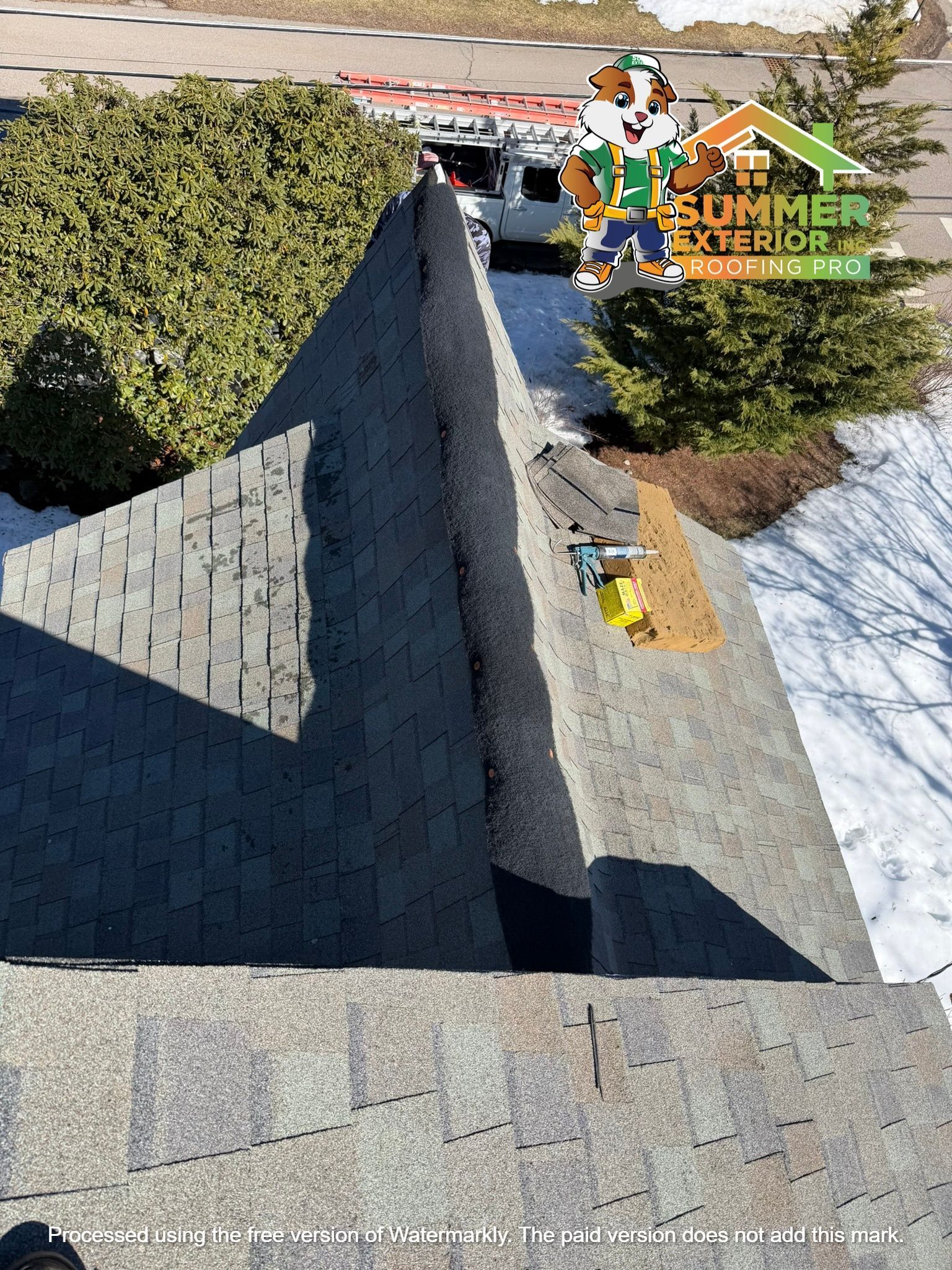 High-angle view of a residential roof undergoing repairs, with tools and materials on the shingles near a pine tree.