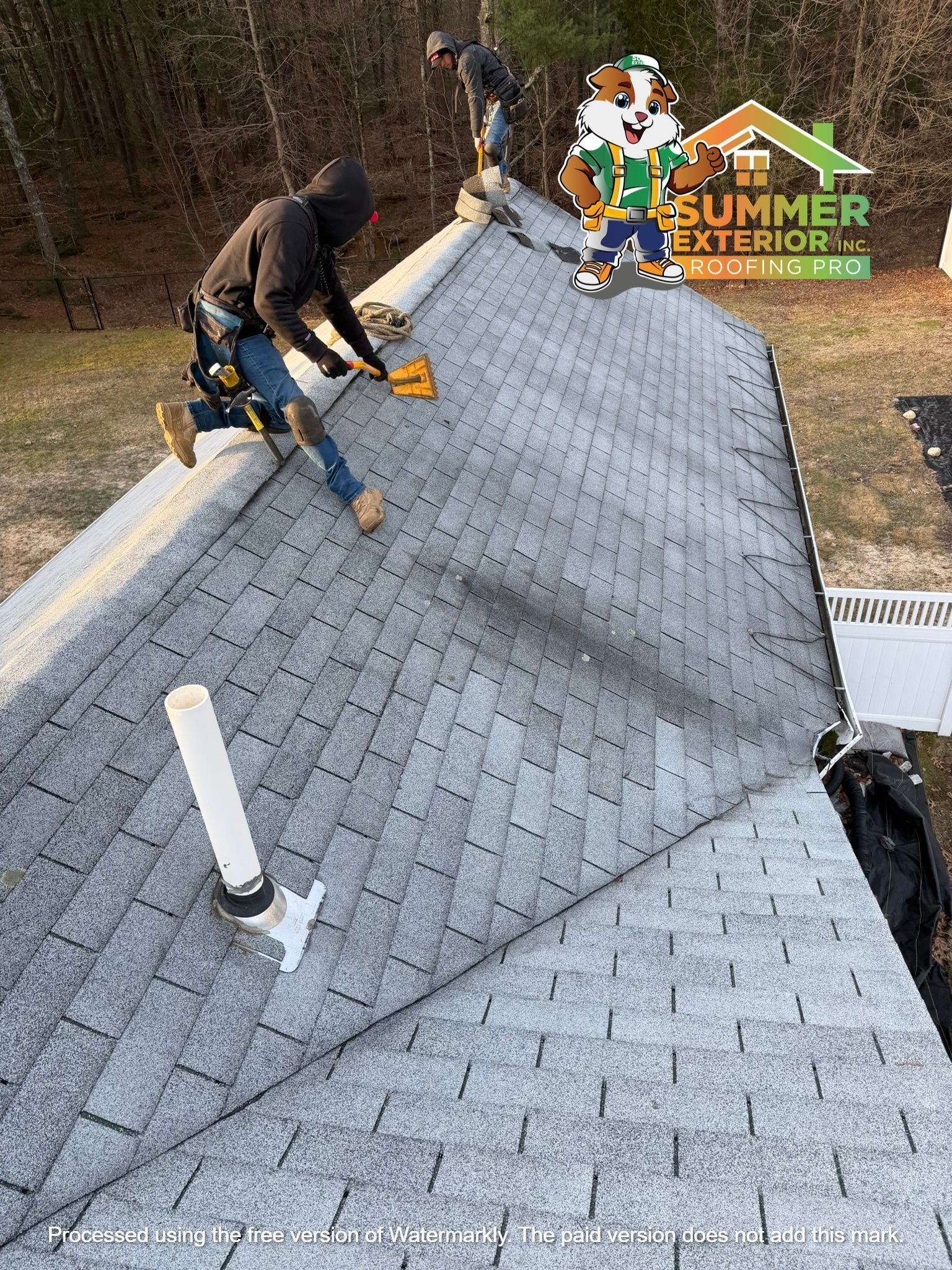 Two people on a residential roof installing shingles, with a cartoon mascot graphic in the corner.