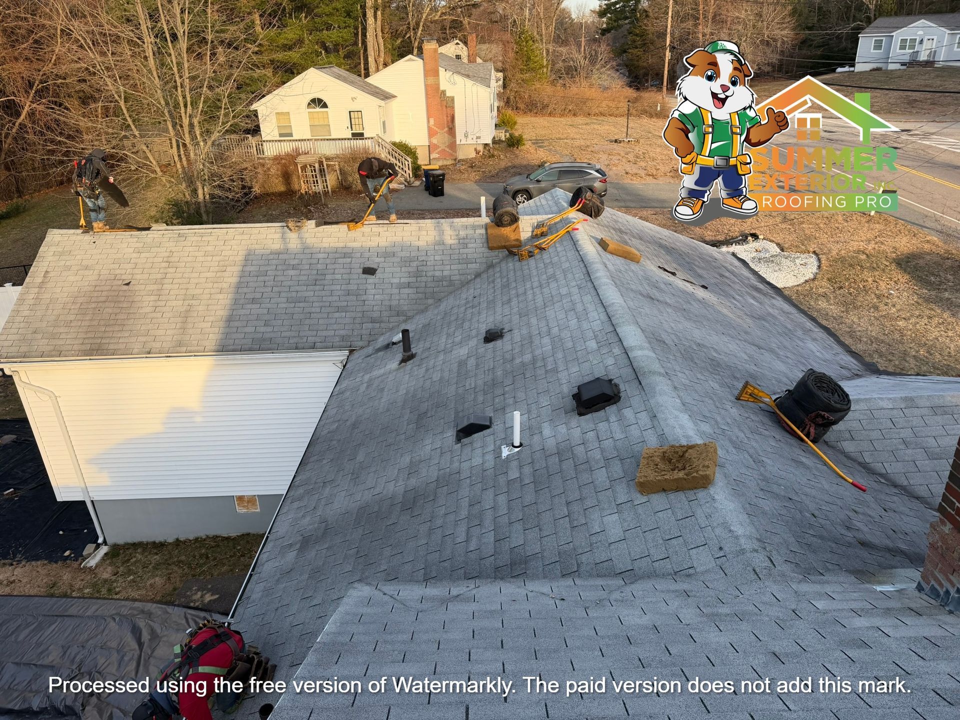 Workers installing gray asphalt shingles on a residential roof.