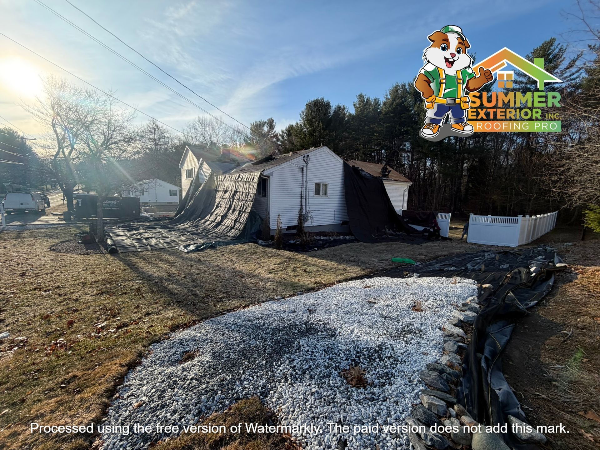 A house exterior under renovation with black ground covering, white landscaping stones, and a Summer Exterior logo.
