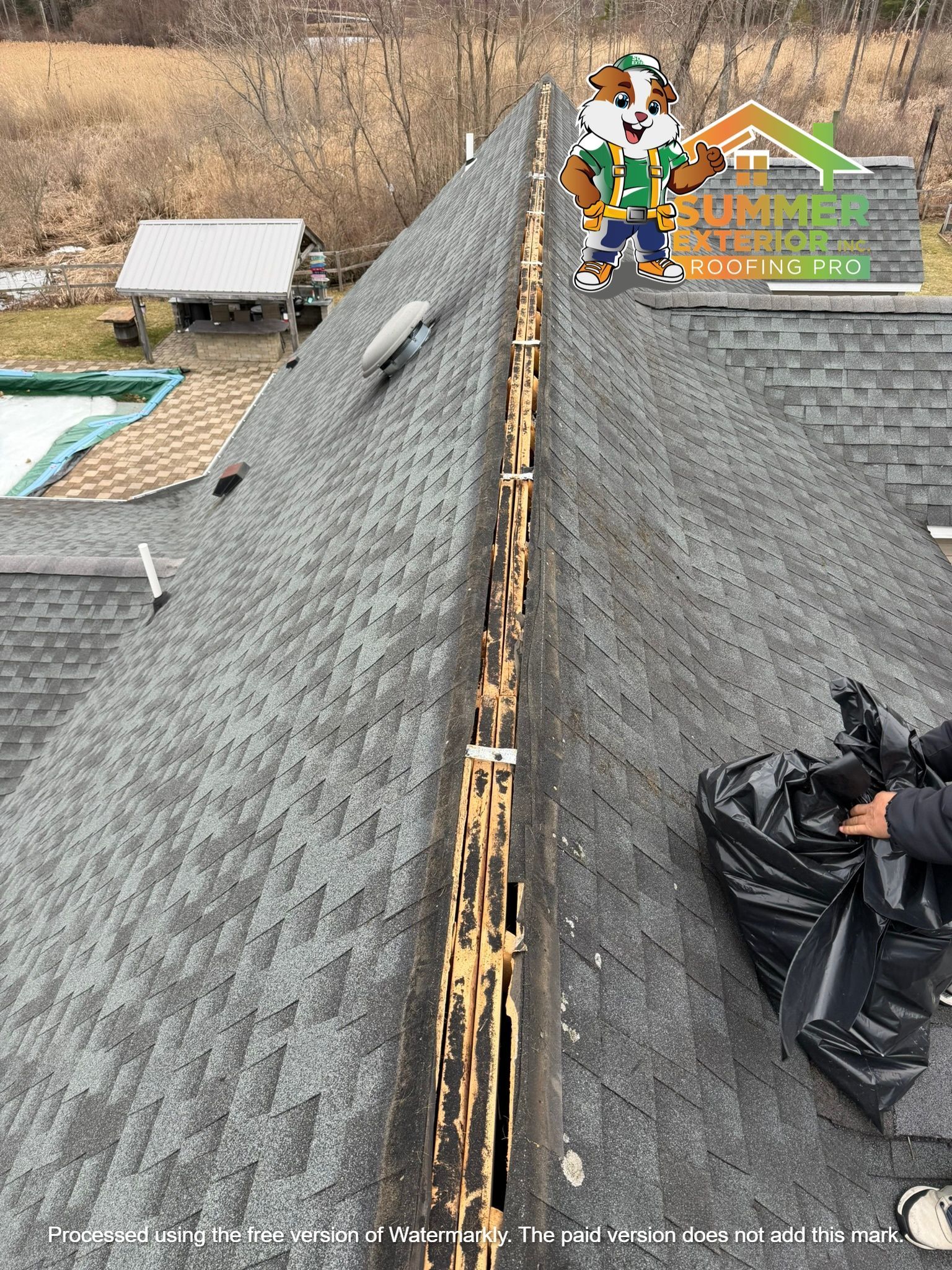 A technician stands on a rooftop, removing shingles to expose the open wooden ridge vent for repair.