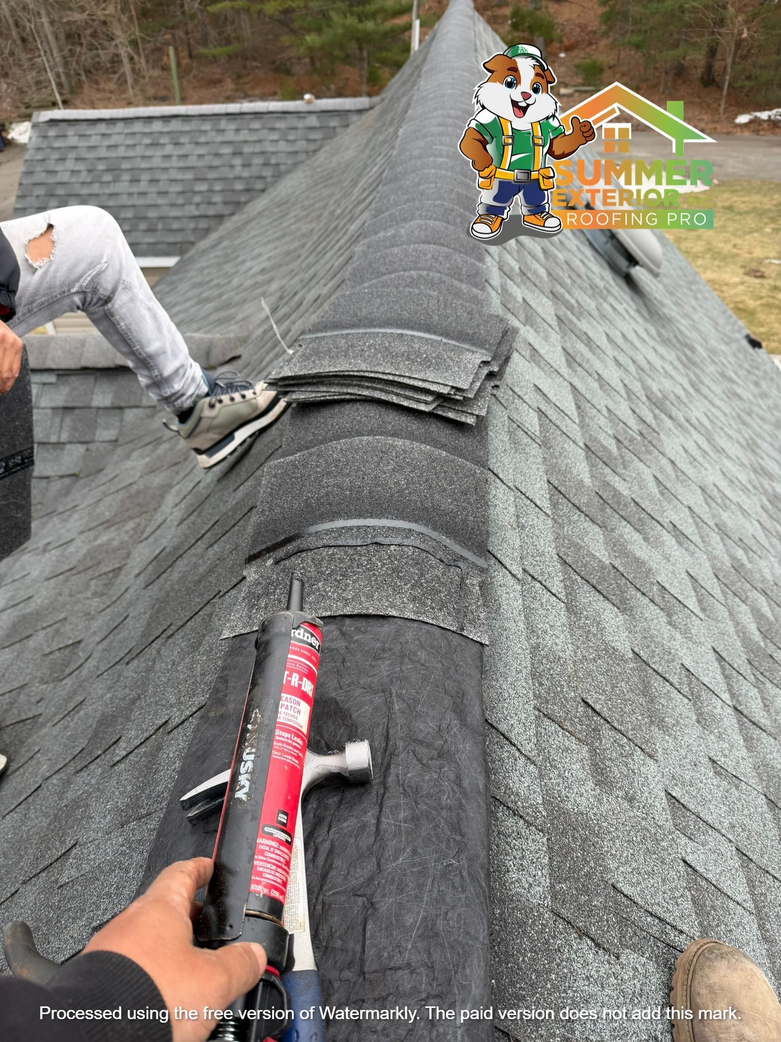 A person repairs a dark shingled roof, holding a tube of sealant with a hammer nearby.